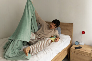 Man in pajamas pulling off the blanket as he gets ready to get out of bed in the morning. Morning routine at home