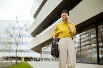 Woman in yellow shirt walks and talks on phone outside modern building