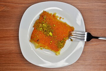Close up of homemade kataifi pastry with syrup and pistachio nuts on a glass plate with fork