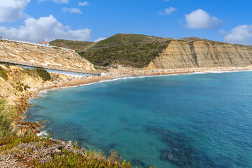 Stunning panoramic view of Praia do Magoito, a beautiful beach in Sintra, Portugal, with golden cliffs, turquoise Atlantic ocean, and summer crowds.