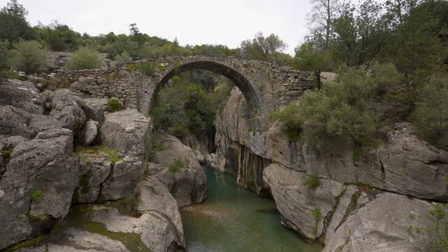 Ancient arch stone bridge spanning a tranquil river in a rugged canyon landscape in Koprulu canyon, Turkey