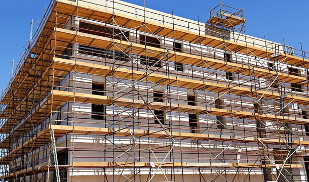Worker installing scaffolding on building, showcasing the teamwork and safety equipment required for scaffold setup on construction site, focusing on safety harnesses and work platforms. - Powered by Adobe