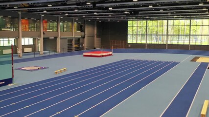 Valmiera, Latvia - May 14, 2019: Indoor athletic facility showcasing blue track and field equipment, camera pans across the spacious arena with natural light