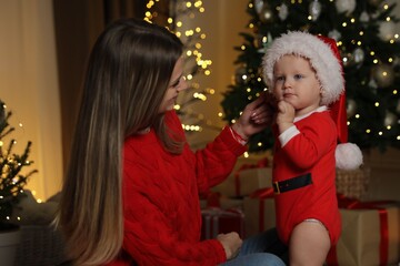 Fototapeta premium Mother with her baby in pajamas and Santa hat near Christmas tree