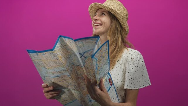 Woman reads a large folded city map held with both hands in a magenta studio setting; curiosity travel exploration.