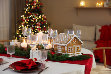 Festive table setting with beautiful gingerbread house against blurred lights indoors. Christmas atmosphere