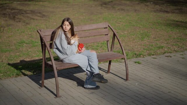 young female gazing thoughtfully with canine companion, young woman sitting beside her dog on quiet park bench, woman relaxes on bench next to paved walkway with her dog during peaceful spring morning