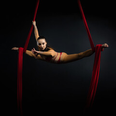 Elegant Aerial Silks Acrobat Performing Dynamic Poses on Red Fabric on Black Background