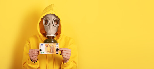Individual in yellow hoodie and gas mask holding fifty euro banknote against solid yellow...