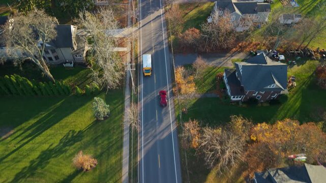 Aerial view of a yellow school bus driving along a suburban street in a typical small American town.
