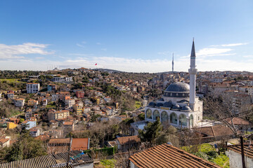 Obraz premium Rooftop view of Çamlıca hills with Haci Mehmet Mosque in foreground, showcasing minarets, houses, and the iconic television tower under a sunny blue sky. Istanbul, Turkey.