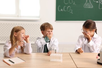 Group of children with test tubes doing chemical experiment and laughing at desk in class. Little scientists