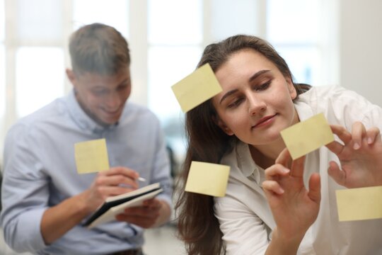 Colleagues discussing strategy near glass board sticky notes in office, selective focus