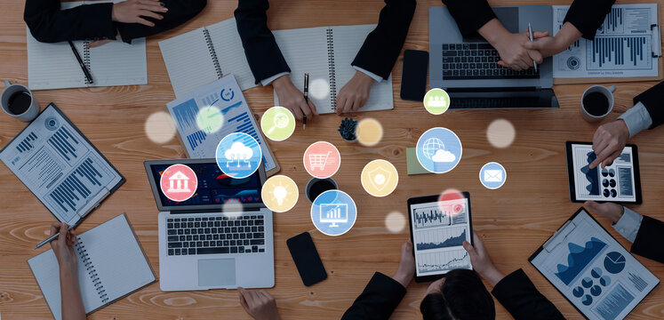 A diverse business team engages in collaborative strategy planning around a table filled with graphs and technology, demonstrating innovation and teamwork. Trope - Powered by Adobe