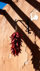 Dried red chili pepper bunch hanging from wrought iron hook on sun-bleached adobe wall