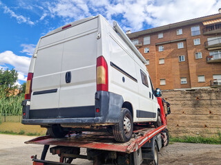 Rear view of tow truck carrying a broken down camper van