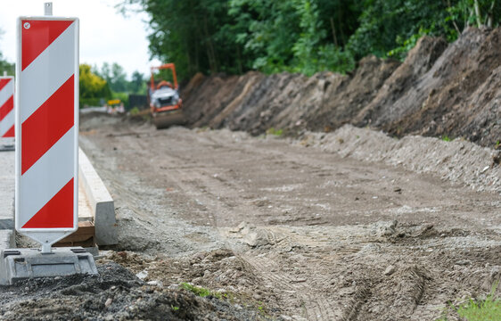 Detail Blick auf eine Stra&szlig;enbaustelle mit laufenden Sanierungsarbeiten an aufgerissener Stra&szlig;e mit Copy Space im Vordergrund, Baumaterial, Absperrung, Maschinen und Erdarbeiten , selektiver Fokus