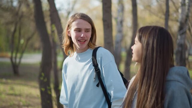 teenagers walking under sunny trees, classmates exchanging smiles amid vibrant spring park surroundings, young friends sharing joyful times outdoors beneath bright sunlight and lush greenery