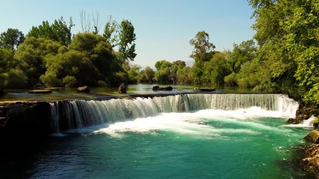 View of Manavgat Waterfall from above in the National Park on a sunny summer day. Unique azure watercolor color with splashes. A wide stream of water falls from a low height. Antalya, Dron, 4K
