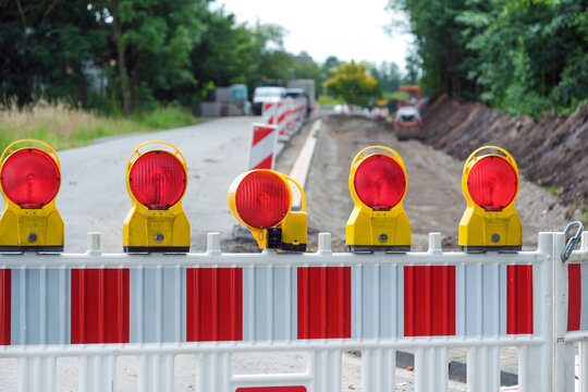 Detail Blick auf eine Absperrung einer Stra&szlig;enbaustelle mit Sanierungsarbeiten an aufgerissener Stra&szlig;e, Baumaterial, Absperrung, Maschinen und Erdarbeiten, selektiver Fokus