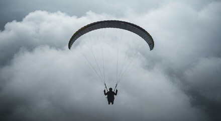 Rear view of paraglider drifting into thick misty clouds at high altitude.