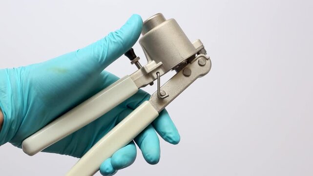 a scientist's hand holding a manual vial crimper, clearly showing the crimping head for sealing aluminum caps onto glass autosampler vials in a laboratory.