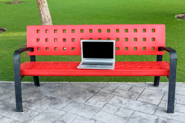 Laptop on a red park bench in a green outdoor setting for work or study