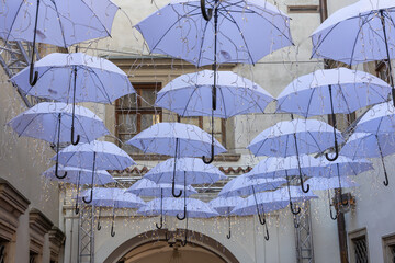 Art installation of hanging blue umbrellas with fairy lights in an alleyway. A low-angle view of a creative art installation