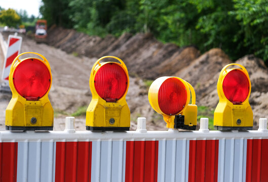 Detail Blick auf eine Absperrung einer Stra&szlig;enbaustelle mit Sanierungsarbeiten an aufgerissener Stra&szlig;e, Baumaterial, Absperrung, Maschinen und Erdarbeiten, selektiver Fokus