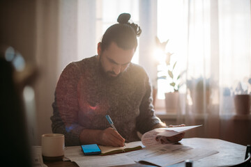 A man sitting at a table with utility bills in his hands.  A man calculates the increased costs of...