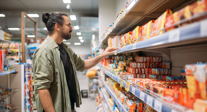 A young man is shopping at the supermarket. A guy walks with a cart between the counters in a big store