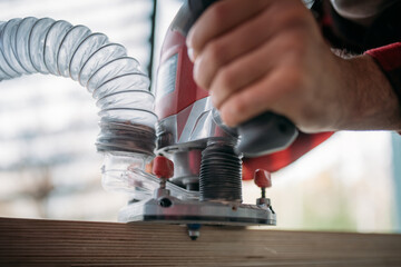 A young man is working with a milling cutter on the veranda of a house. Close-up of hands holding the machine. The carpenter is chamfering plywood using the milling machine.