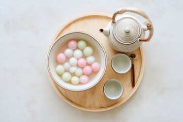 Tang yuan dessert with colorful glutinous rice balls in sweet syrup served in bowl on wooden tray with teapot and cups creating cozy and inviting atmosphere