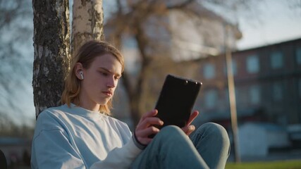 youth engaging with digital content outside, young person absorbed in tablet outdoors under sunset, student enjoying instructional material on tablet amidst scenic outdoor setting at dusk