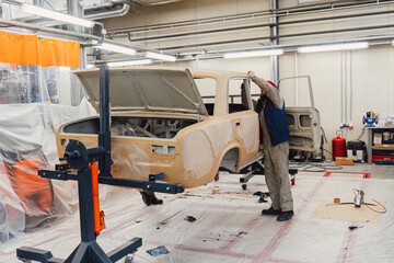 Specialist spraying anti rust sealant into the hidden chassis cavities. Protection against corrosion and internal body element sealing in a professional auto service shop
