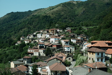 Traditional mountain village in Northern Spain, surrounded by green forested mountains and blue sky. Film-like colors create a soft, atmospheric feel