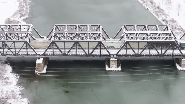 Railroad train industrial and steel metal bridge by downtown area across and over the Scioto Mile river with frozen water during a snowy winter storm and snow covered season from a drone shot aerial