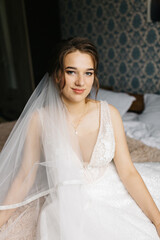 Bride smiling softly as her veil flows around her, creating a dreamy and romantic atmosphere. The close-up portrait highlights her makeup, lace wedding dress, and elegant jewelry in gentle natural 