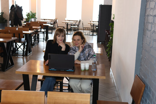 Two women working on a laptop while sitting at a table in a cafe
