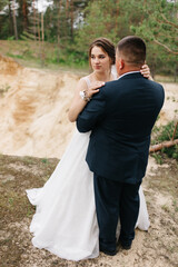 The bride gently embraces the groom, smiling and looking into his eyes. The forest background highlights sincere emotions, warmth, and intimacy of this special wedding moment.