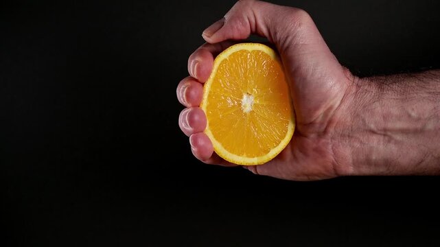 male hand squeezing half an orange against black