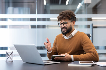Young businessman engaged in a virtual conference, using a laptop for remote work communication and participating in an online meeting from a modern office environment