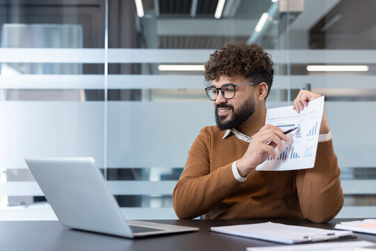 Man pointing at a financial chart on paper, explaining data and business analytics during a professional online remote video conference from an office workspace
