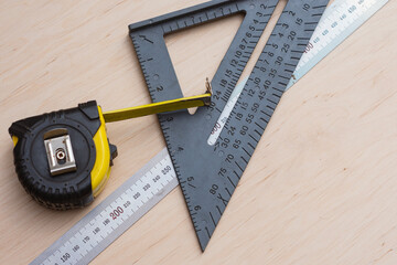 Measuring tape with construction square and metal rulers arranged on a wooden surface. Concept precision and professional carpentry tools for woodworking and technical measurement themes.