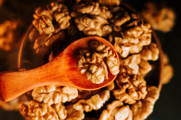 Peeled walnuts in a wooden bowl with a spoon on a dark surface