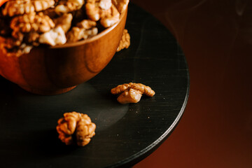 Peeled walnuts on a dark wooden table near a bowl filled with nuts