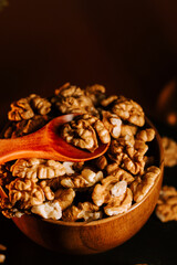 Peeled walnuts in a wooden bowl with a spoon on a dark background
