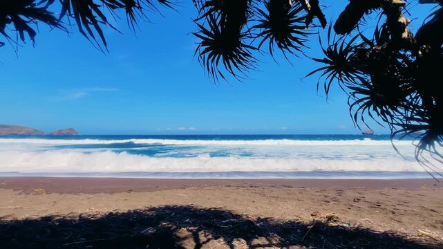 The sea in Jember, East Java. Indonesia. Watu Ulo beach with dark sand, mountains and coral rocks towering above the beach. The raging blue Indian ocean on a sunny day. 4К