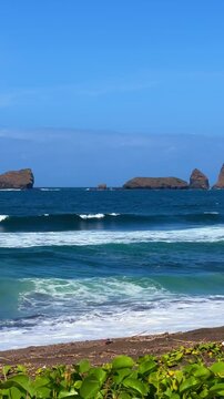 The sea in Jember, East Java. Indonesia. Watu Ulo beach with dark sand, mountains and coral rocks towering above the beach. The raging blue Indian ocean on a sunny day. 4К