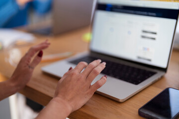 A person's hands are shown interacting with a laptop and a smartphone on a wooden desk, suggesting digital work or communication.